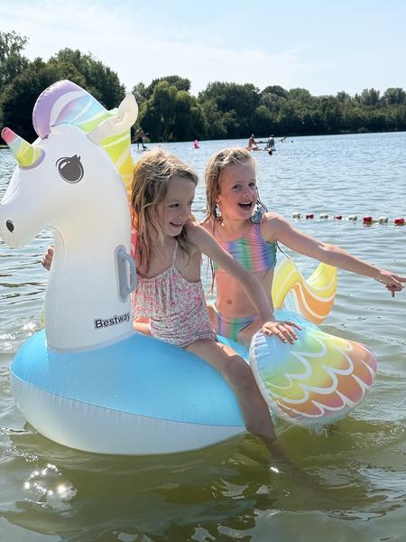 Two young girls play on a unicorn shaped float in a lake on a sunny day